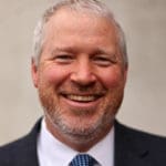 Photo headshot of Mike McGinn on a beige background.