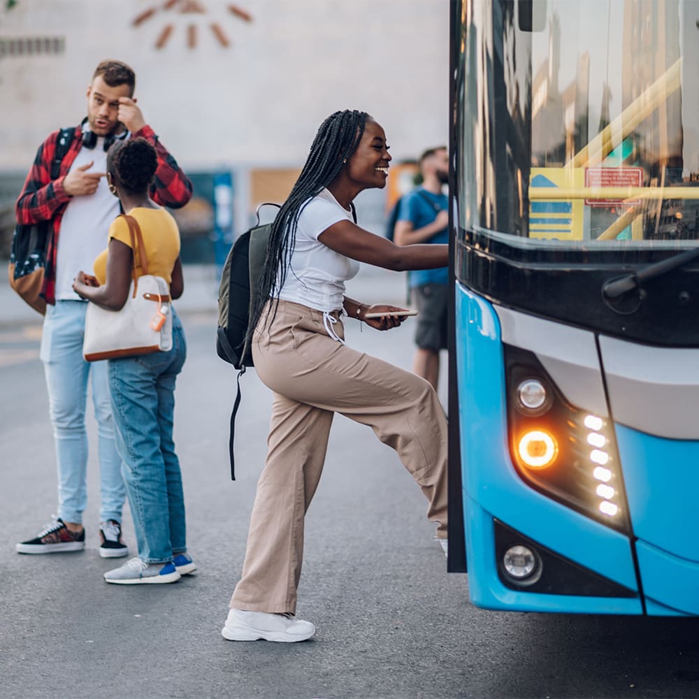 Multiracial passengers waiting at a bus stop and talking cheerfully. Focus on an african american woman entering the bus. Diverse tourists in new town. Best friends traveling together in a city.