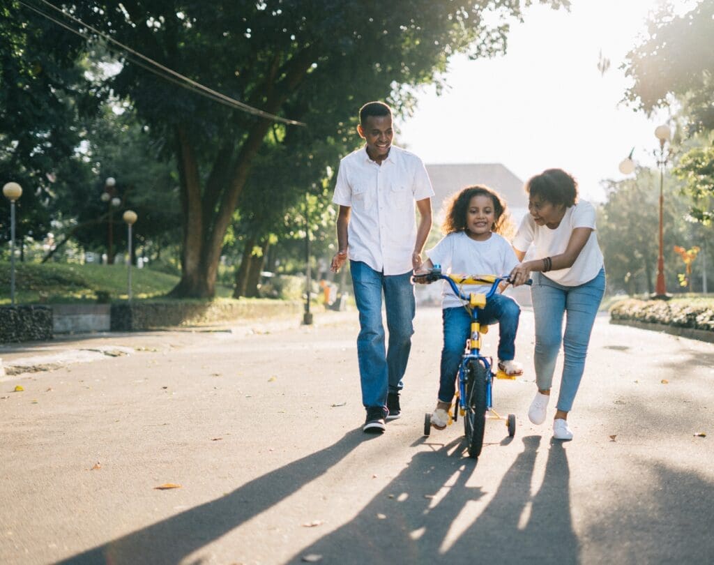 Two people helping a young child ride a bike in the middle of the street.