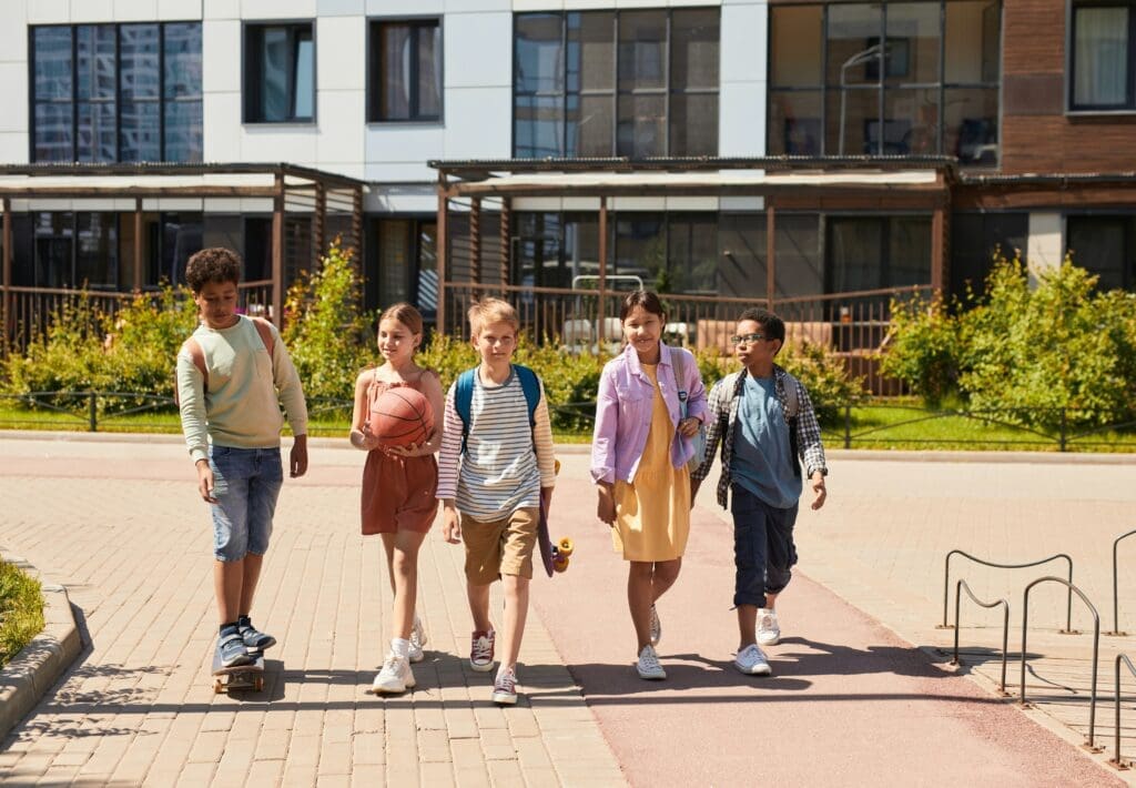 5 children, 4 walking 1 on a skateboard on a walking path