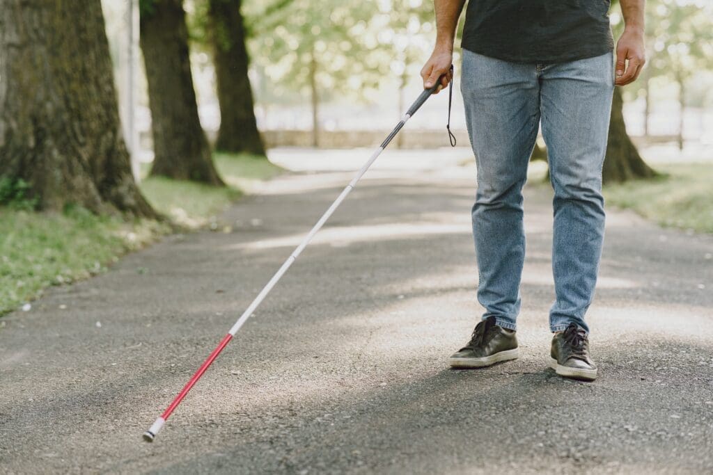 A blind man walks through a park.