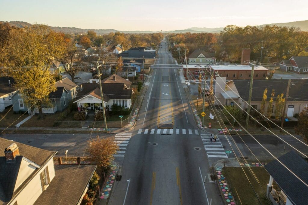 Flyover photo of a street demonstration project with bike lanes, sidewalk art, and crosswalks. Funding for active transportation includes demonstration projects.