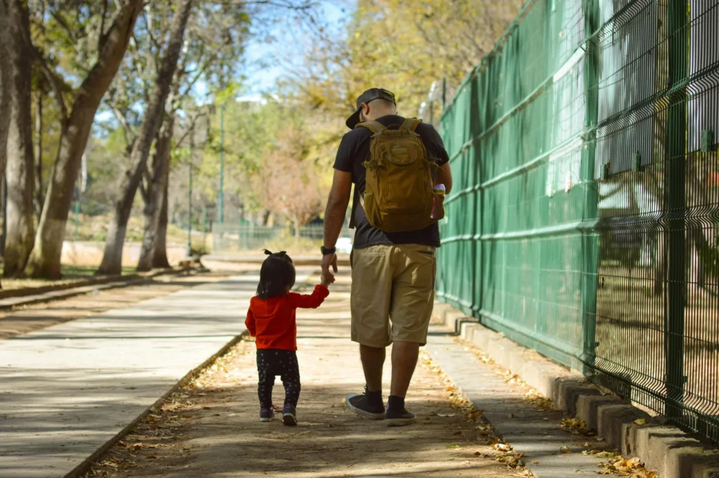 a child and father walk hand in hand on a sidewalk