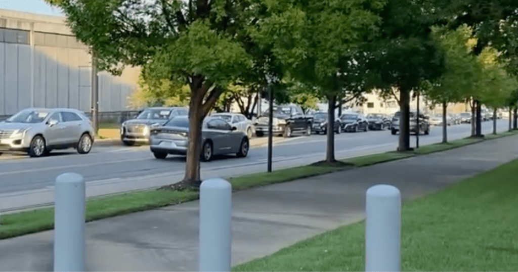 Cars idle as far as you can see taking up the road near a school.