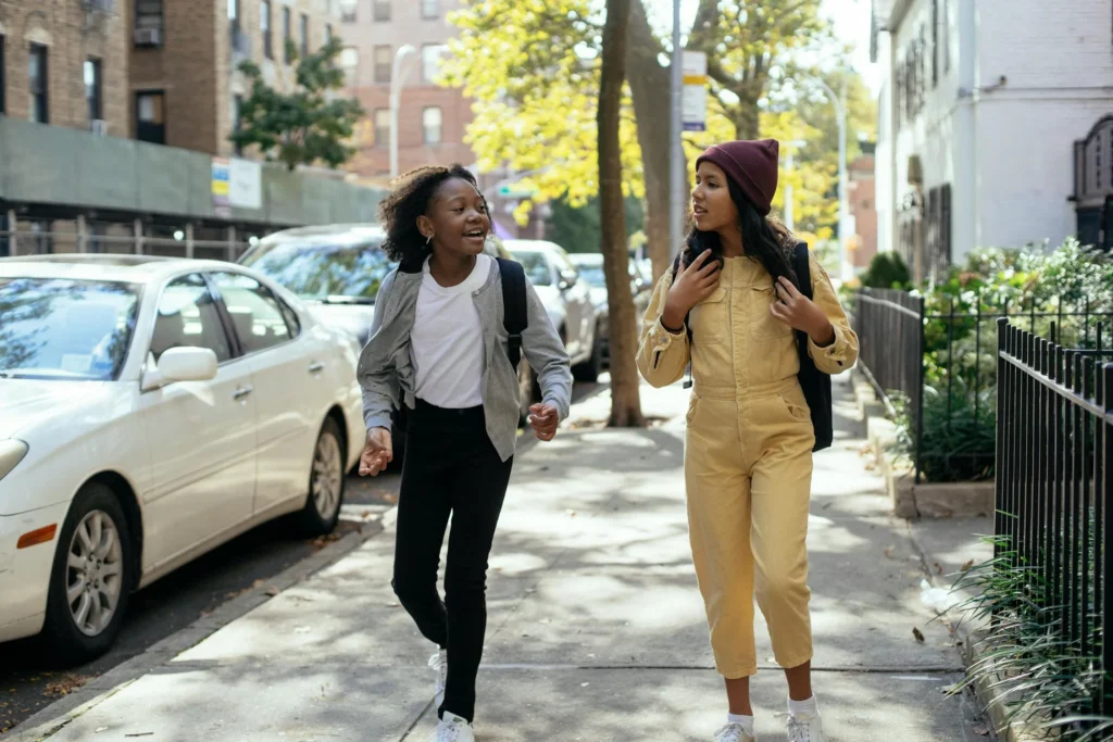 Two young people chatting while walking on a sidewalk on a sunny street.