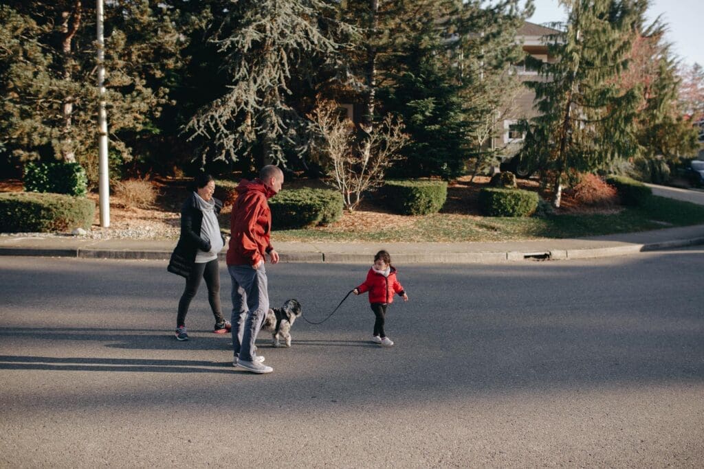 a child holding a leash of a dog walking in the middle of the street with two adults