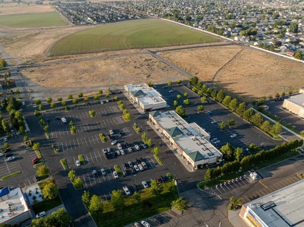 two buildings with a few shops are surrounded by a 75% empty parking lot