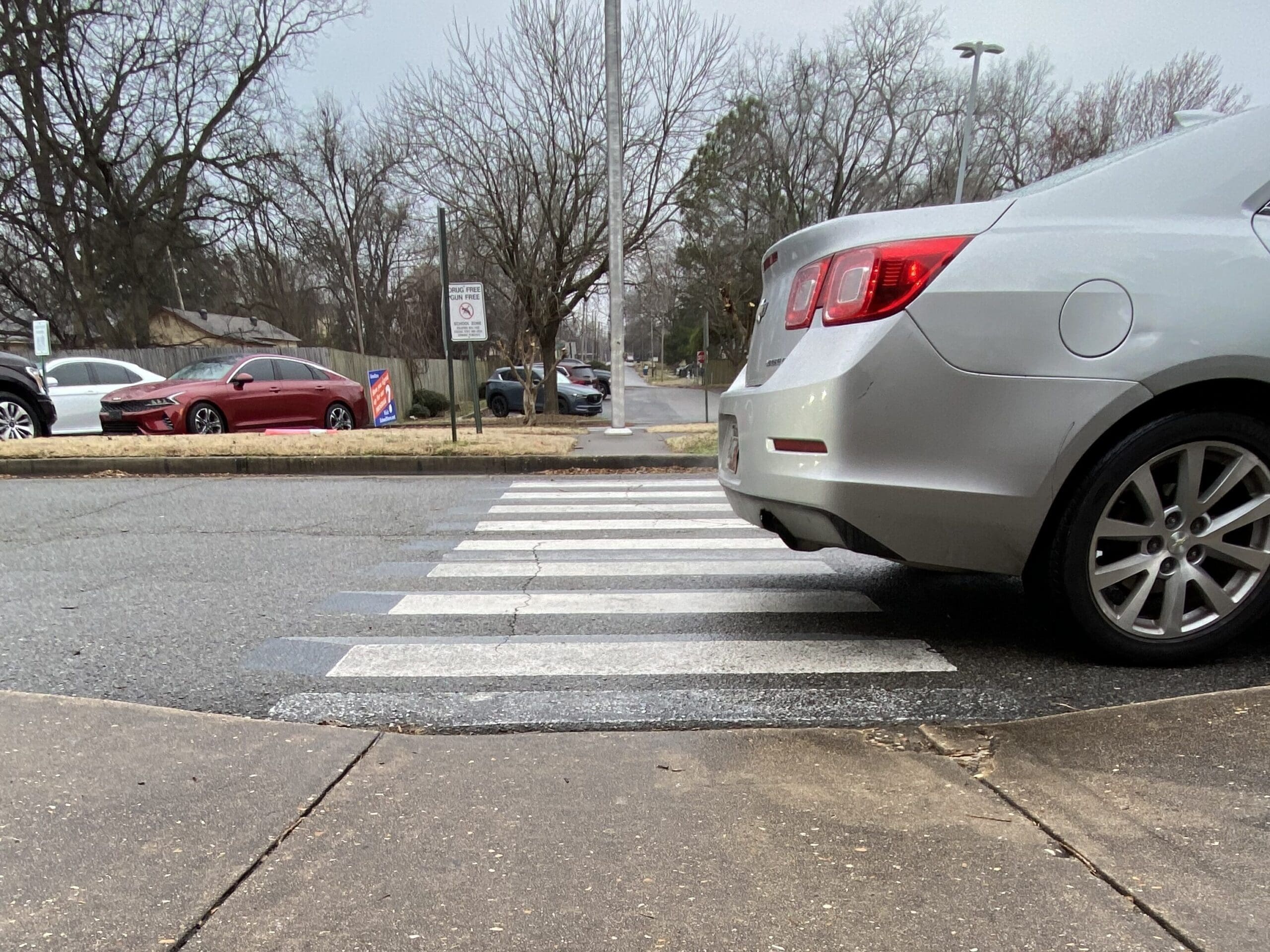 an image of a car who's back is parked over the crosswalk, cutting of part of the walking path for those who need to cross. the other side of the crosswalk does not have ramp.